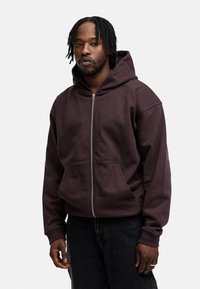 Brauner Zip-Hoodie mit großer Fronttasche, aus weichem Stoff, mit Kapuze und lässiger Passform. Ideal zu dunklen Jeans.