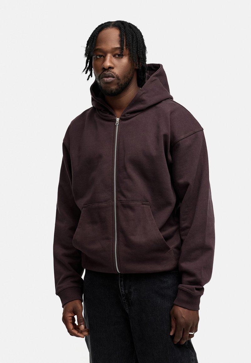 Brauner Zip-Hoodie mit großer Fronttasche, aus weichem Stoff, mit Kapuze und lässiger Passform. Ideal zu dunklen Jeans.
