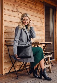 Černá kožená kabelka přes rameno se stříbrným logem, obdélníkový tvar, hladká textura. Šedý kabát, zelené žebrované šaty a černé podpatky.