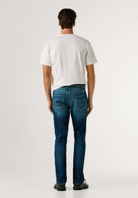 Camiseta blanca de manga corta combinada con vaqueros de mezclilla azul. Los vaqueros presentan un corte clásico con dos bolsillos traseros y una pretina oscura.