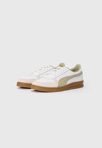 Baltas sneakerus ar zaļiem akcentiem un bēšiem zamša paneļiem. Apaļa purngalu forma, plakana šņorēšana un gumijas zole. Tīrs dizains ar perforācijām.