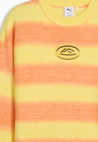 Zachte gebreide trui met brede horizontale gele en oranje strepen en een klein ovaal patchlogo op de borst.