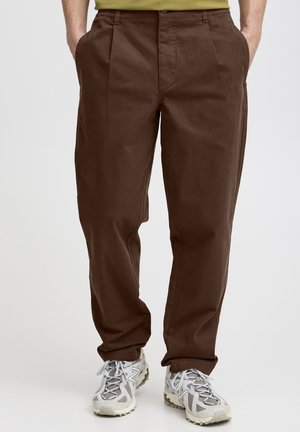 Brown cotton trousers with a relaxed fit, featuring front pleats and side pockets, paired with light gray athletic shoes.
