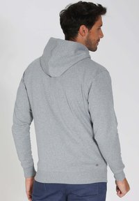 Sweat à capuche gris avec cordon de serrage, manches longues et ourlet et poignets côtelés. Texture lisse avec un petit logo en bas.