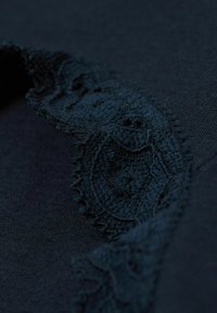 Mörkblå textil med en delikat spetskant med vågig kant, som visar upp intrikata mönster och en texturerad yta.