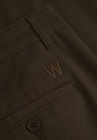 Brown fabric with stitched detailing and a pocket. Features a brown embroidered "W" logo. Includes a brown button and stitching.