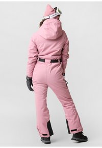 Pink ski suit with black accents, featuring a belted waist, hood, and gloves. Includes zippers on the pants. Worn with a pink beanie and goggles.