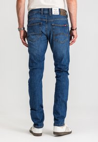 Niebieskie dżinsy z prostą nogawką, średnim stanem, kontrastującymi przeszyciami i charakterystycznymi tylnymi kieszeniami. Noszone z białymi trampkami.