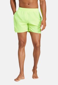 Costume da bagno verde lime con cintura elasticizzata, tasche laterali e vestibilità comoda. Tessuto liscio con una texture leggera.