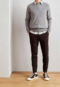 Grå tröja över en vit och blå rutig skjorta, parat med skräddarsydda svarta byxor och svarta sneakers med vita sulor och snören.