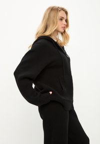 Černá pletená mikina s uvolněným střihem, s žebrovanými manžetami a přední kapsou, s kapucí na šňůrku a měkkou texturou.