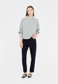 Grijze trui met verlaagde schouders, geribbelde manchetten en een klein logo, gedragen over een lichtblauw overhemd met kraag, gecombineerd met marineblauwe broek.