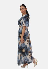 Maxi kjole med et blomstermønster i blå og beige nuancer, kortærmede og med en smocked talje. Båret med beige strop sandaler.