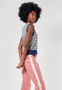 Knit sleeveless top with a geometric pattern in blue, pink, and cream. Paired with pink pants featuring white side stripes. Smooth texture.