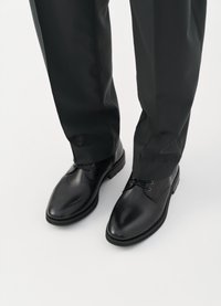 Pantofi negri din piele cu un finisaj neted, vârf rotund și design cu șireturi, asortați cu pantaloni dark ajustați, pe un fundal alb.