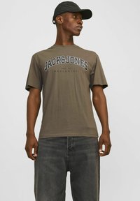 Oliven grøn t-shirt med rund halsudskæring og korte ærmer, prydet med fed, sort tekst "JACK&JONES" og etableringsdatoen nedenunder.