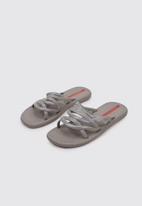 Chanclas de color gris claro con una suela suave y texturizada, y múltiples correas trenzadas. Detalle del logo rojo en la plantilla.