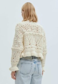 Cremfarbener, gestrickter Pullover mit offenem Maschenmuster, kürzerer Länge, gerippten Bündchen und einem strukturierten, gemütlichen Look, kombiniert mit hellblauen Jeans.
