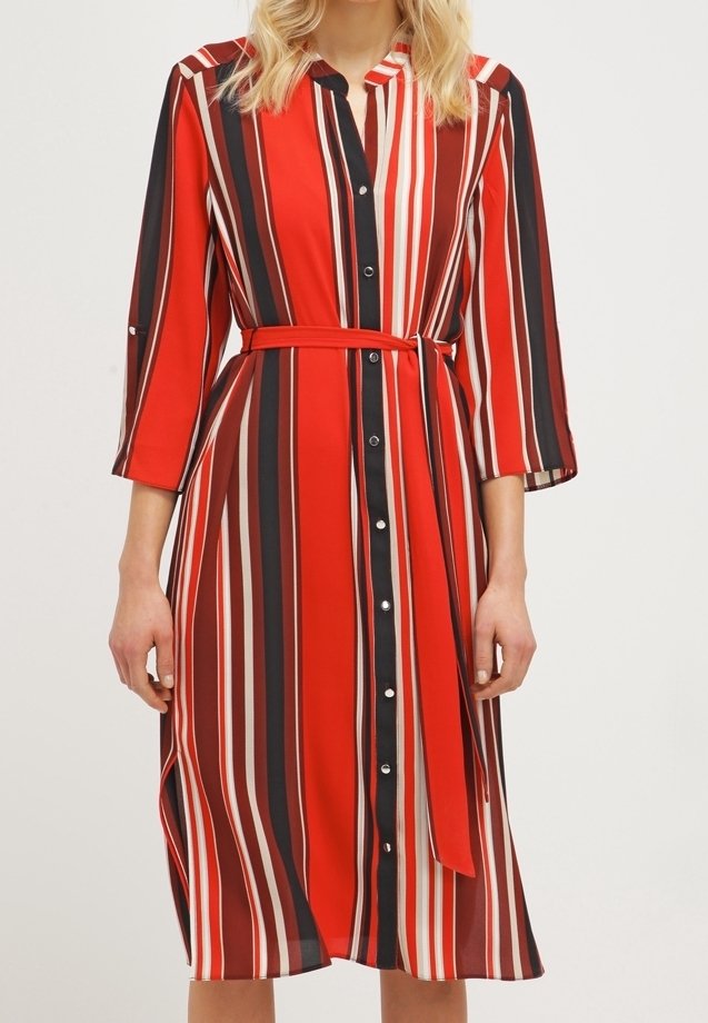 Femme portant une robe midi boutonnée et ceinturée à rayures verticales rouges, noires, blanches et marron, avec des manches trois-quarts.