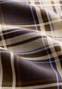 Tissu à carreaux marron et crème avec des lignes bleues, présentant un motif texturé et un tombé doux, mettant en valeur des motifs de carreaux entrelacés.