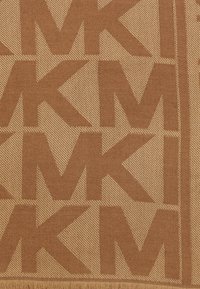 Tessuto tessuto color sabbia con un motivo ripetuto "MK". La texture è morbida con una leggera lucentezza, incorniciata da una frangia nella parte inferiore.
