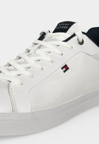 Baskets en cuir blanc Tommy Hilfiger avec lacets blancs, col noir et petit logo rouge, blanc et marine sur le côté.