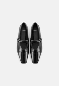 Sapatos de verniz pretos com biqueira pontiaguda, tira sobre o peito do pé e acabamento brilhante. Design simples com um detalhe de fivela.