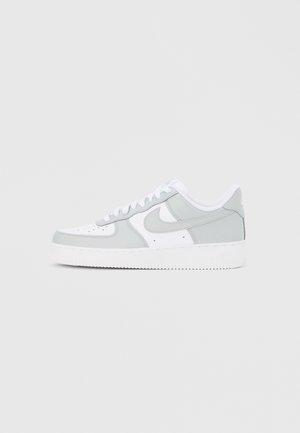Basket basse Nike blanche et gris clair avec un laçage et une semelle blanche épaisse, montrée de profil sur un fond clair.