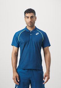 Tumed sinine sportlik polo-särk lühikeste varrukatega, tekstureeritud kangas, rohelised aksendid õlavartel ja väike logo rinnal.