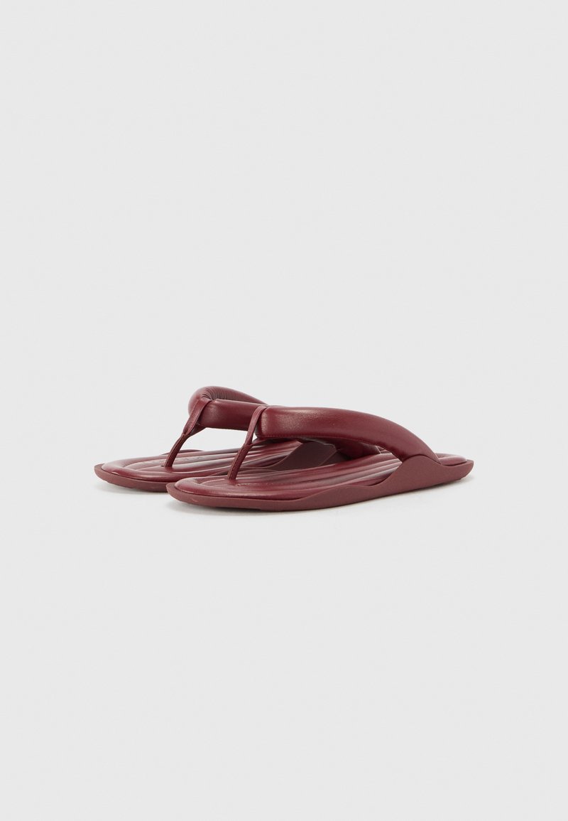 Flip-flops in a deep burgundy color, made of flexible rubber. Features a textured footbed with raised lines and a minimalist strap design.