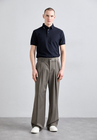 Marinblå pikétröja med korta ärmar och knapplist, kombinerad med höga grå veckade byxor och vita sneakers.