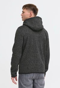 Tumehall hall knitted kapuuts, millel on tekstureeritud viimistlus, koos nööriga kapuuts ja pikad varrukad, kantud heleshallide teksade üle.