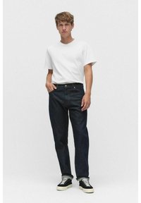 Mörkblå denimjeans med avslappnad passform, uppkavlade fållar och femfickorsdesign, i kombination med en enkel vit t-shirt och svarta sneakers.