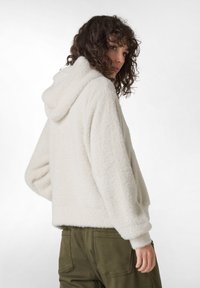 Witte nepbont hoodie met een capuchon, relaxte pasvorm, ribgebreide manchetten en onderkant. Gepaarde met olijfgroene broek. Gelaagd, warm uiterlijk.