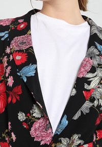 Sako s květinovým vzorem na černém pozadí. Obsahuje živé rudé, růžové a modré květy. Noste přes bílé tričko s kulatým výstřihem.