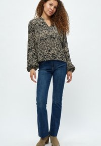 Blusa nera e beige a fantasia con scollatura a V e maniche a sbuffo, abbinata a jeans svasati blu scuro e stivaletti alla caviglia color cammello.