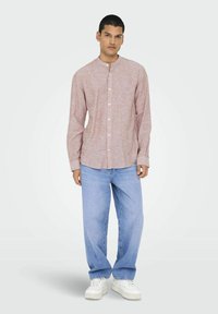 Camicia button-up rosa chiaro con colletto alla cinese, maniche lunghe e tessuto testurizzato, abbinata a jeans larghi azzurri e sneakers bianche.