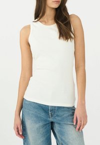 Top senza maniche a costine di colore bianco sporco, con scollo rotondo e delicata ricamo frontale. Abbinato a jeans in denim azzurro chiaro a vita alta.
