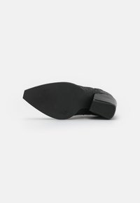 Zapato negro tejido con una superficie texturizada, que cuenta con una suela negra sólida y un tacón medio en bloque. El diseño es elegante y moderno.