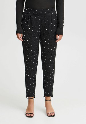 Schwarze Hose mit einem dehnbaren Bund, verziert mit einem Muster aus kleinen weißen Herzen. Schmal zulaufendes Bein mit Schlitzen an den Knöcheln, aus softem Material gefertigt.