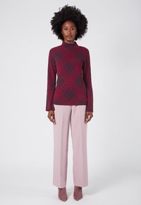 Maglione bordeaux a fantasia con texture a coste, colletto alto, abbinato a pantaloni palazzo rosa chiaro e stivaletti taupe.