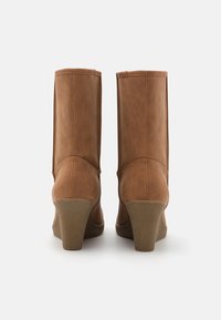 Bottes cheville en similicuir marron avec un talon haut effilé et une texture lisse. La tige présente un design sans coutures avec une bordure cousue.