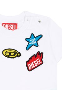 Maglietta bianca in cotone con tre toppe ricamate: una stella blu, un ovale giallo e una fiamma rossa con la scritta "DIESEL" in bianco.