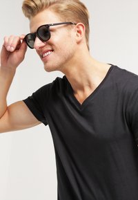 Black V-neck t-shirt made of soft fabric; model wearing black sunglasses while adjusting them, showcasing a relaxed fit and smooth texture.