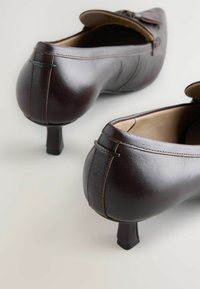 Braune Lederschuhe mit einem niedrigen Absatz, runder Spitze und dekorativem Schleifenakzent. Glatte Textur und dezente Steppdetails.