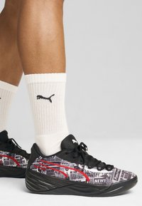 Scarpe sportive nere con una stampa di giornale, dettagli rossi e lacci neri. Abbinate a calze bianche a costine con un logo nero.