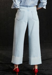 Jeans de pierna ancha en azul claro con dobladillo deshilachado, confeccionados en denim, con bolsillos traseros y combinados con unos zapatos de tacón rojos.