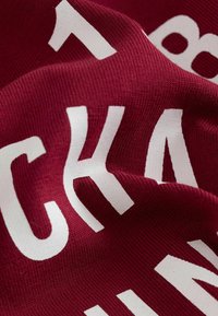 Teren de Burgundy cu o textură în dungi, afișând litere albe îndrăznețe, scrise cu litere mari. Designul prezintă culori contrastante și un text proeminent.