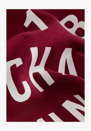 Burgundia kangas ribakujulise tekstuuriga, millel on julged valged plokktähed. Kujundusel on kontrastsed värvid ja silmapaistev tekst.