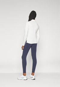 Vit långärmad topp, figurnära marinblå leggings och vita sportskor med silverdetaljer. Toppen har sidofickor för ökad komfort.